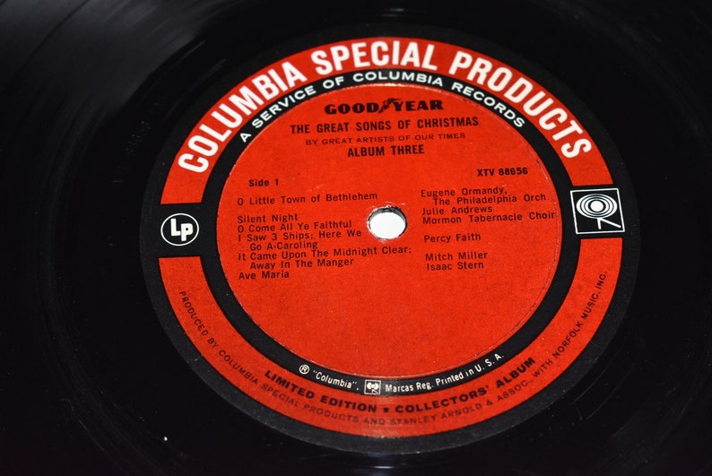 May include: A red vinyl record with a black label. The label features the text "Columbia Special Products", "A Service of Columbia Records", "Good Year", "The Great Songs of Christmas", "By Great Artists of Our Times", "Album Three", "XTV 88656", "Side 1", "O Little Town of Bethlehem", "Silent Night", "O Come All Ye Faithful", "I Saw 3 Ships, Here We", "Go A-Caroling", "It Came Upon The Midnight Clear", "Away In The Manger", "Ave Maria", "Eugene Ormandy, The Philadelphia Orch", "Julie Andrews", "Mormon Tabernacle Choir", "Percy Faith", "Mitch Miller", "Isaac Stern", "Limited Edition Collectors' Album", "Columbia", "Marcas Reg. Printed in U.S.A.", and "Produced by Columbia Special Products and Stanley Arnold & Assoc. with Norfolk Music, Inc.".