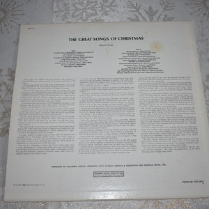 May include: The back of a vinyl record album titled "The Great Songs of Christmas". The album cover is white with black text. The album features a list of songs on each side of the record. The album is produced by Columbia Special Products with Stanley Arnold & Associates and Morriss Music, Inc.