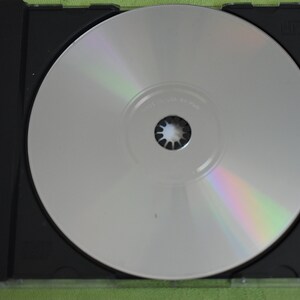 May include: A silver CD in a black jewel case. The CD has a rainbow iridescent sheen.