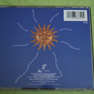 May include: A blue CD case with a sun graphic and the text "Woman in Chains" and "Badman's Song". The CD case is for the album "Standing on the Corner of the Third World" by the band "The Alarm".