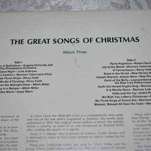 May include: A white and black album cover with the title "The Great Songs of Christmas" and a list of songs on each side of the record. The album is part of a series and is labeled "Album Three".