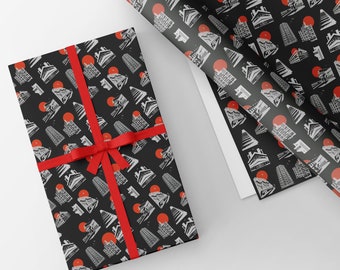 May include: A black and white gift wrap with a repeating pattern of red suns and buildings. The gift wrap is rolled up and tied with a red ribbon.
