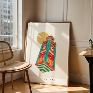 May include: A framed art print depicting a vibrant illustration of a clock tower, set against a yellow sun. The clock tower is rendered in red, teal, and gold. The print is propped against a wall, beside a window and a wooden chair.