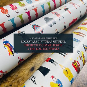 May include: Three rolls of white gift wrap featuring illustrations of musicians, including The Beatles, David Bowie, and The Rolling Stones. The text on the wrapping paper reads "Rockstars Gift Wrap Set Feat. The Beatles, David Bowie & The Rolling Stones".