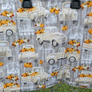 May include: Fabric with a repeating pattern of vintage cream-colored trucks filled with pumpkins and white gourds. The background is a gray wood grain design. Text includes "Farm Fresh", "Pumpkin Patch", and "Pick Your Own".