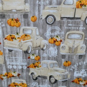 May include: Fabric with a repeating pattern of vintage cream-colored trucks filled with orange and white pumpkins. The background is a gray wood grain texture, with text that reads "Pumpkin Patch" and "Farm Fresh".
