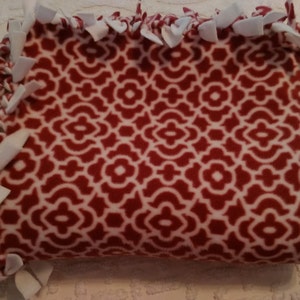 May include: A red and white fleece blanket with a geometric pattern. The blanket is tied with white fabric ties.