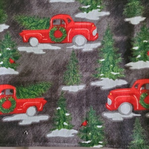 May include: Red pickup trucks carrying Christmas trees on a dark gray background with white snow and green trees. The trucks have red wreaths on the front. The background has the text "Silent Night" in white.