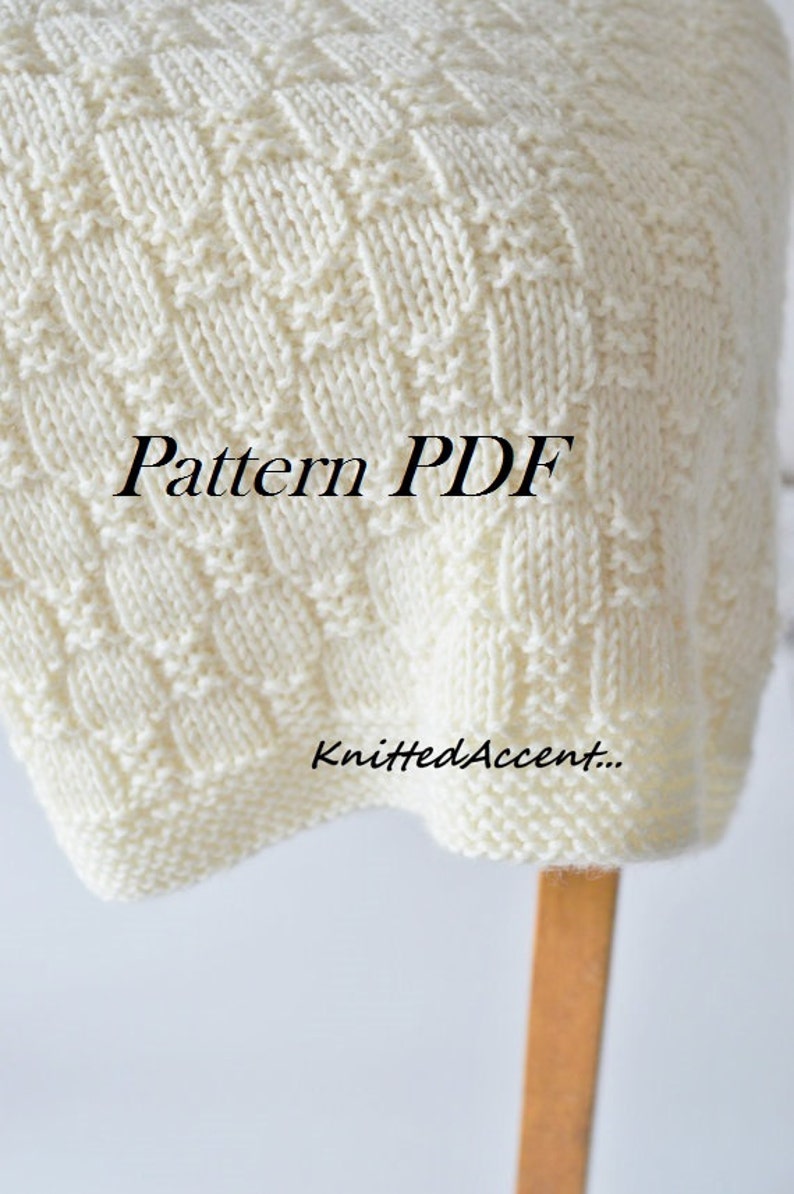 Puede incluir: Una manta de punto blanco con un patr&oacute;n de rombos. La manta est&aacute; doblada y drapeada sobre una silla de madera. El texto "Pattern PDF" est&aacute; impreso en la manta. El texto "KnittedAccent..." est&aacute; impreso en la manta.