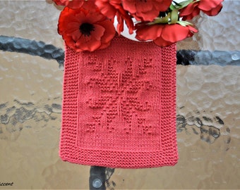 May include: A pink knitted dishcloth with a floral design. The dishcloth is made with a simple stitch pattern and has a square shape.