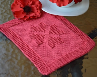 May include: A pink knitted dishcloth with a heart design. The dishcloth is made with a textured stitch and has a border around the edges.