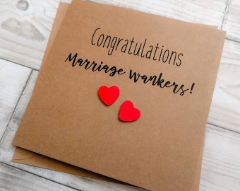 May include: A brown card with the text "Congratulations Marriage wankers!" in black script. Two small red heart-shaped embellishments are below the text. The card is on a light wood grain surface.