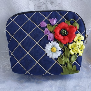 以下が含まれることがあります： 金色の格子模様とリボン刺繍でできた花柄が施された青いジッパー付きポーチ。花は赤、白、黄、紫です。
