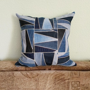Könnte beinhalten: Ein blaues Jeans-Kissen mit einem geometrischen Muster aus verschiedenen Blautönen von Jeans. Das Kissen liegt auf einem braunen Sofa.
