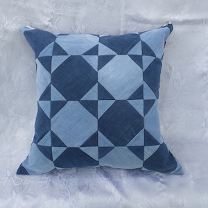 Puede incluir: Una almohada de mezclilla azul con un patrón geométrico de cuadrados y triángulos. La almohada está hecha de mezclilla reciclada y tiene una sensación suave y cómoda.