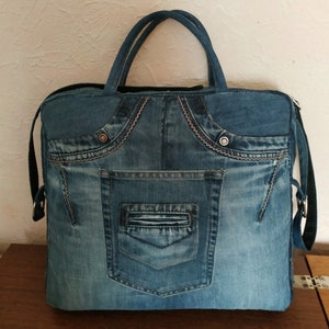 Op de afbeelding: Een blauwe denim draagtas met een groot voorvak. De tas heeft een bovenste handvat en een schouderband.