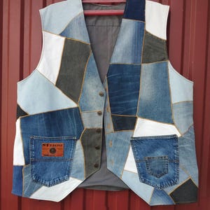 May include: A patchwork denim vest with a variety of blue denim patches, white accents, and a gray interior lining. The vest features two pockets and a button-up front. The label on the pocket reads "ST. LEONE".