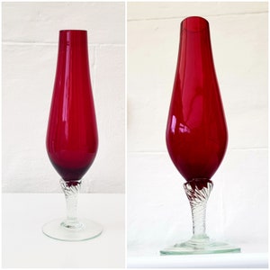 Puede incluir: Un jarrón de vidrio rojo, alto y delgado, con una base de vidrio transparente y un tallo retorcido.