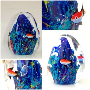 Könnte beinhalten: Ein Glas-Papiergewicht mit einem blauen, grünen und gelben Wirbelmuster. Im Inneren des Papiergewichts befinden sich zwei orangefarbene und weiße Fische.
