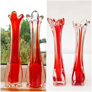 May include: Set of four red and clear glass vases with a unique, wavy design. The vases are tall and slender, with a flared opening at the top.