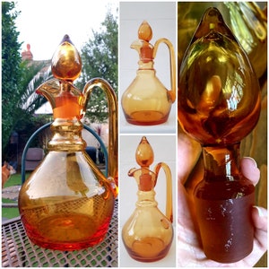 May include: Three amber glass decanters with stoppers. The decanters are all different shapes and sizes. The decanters are on a white background.