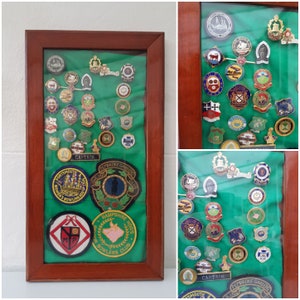 May include: A wooden frame with a green felt background displays a collection of colorful embroidered patches. The patches feature various designs, including a ship, a pig, a crown, and a bowling ball. The text "CAPTAIN" is visible on two of the patches.