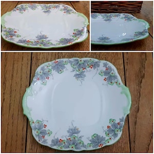 May include: A white ceramic serving plate with a green and grey floral design. The plate has two handles and a raised rim.