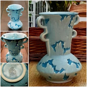 Puede incluir: Un jarrón de cerámica azul claro con un diseño único. El jarrón presenta una base bulbosa, una sección media cilíndrica y una parte superior acampanada con dos juegos de asas curvas. La superficie tiene un aspecto texturizado con acentos azul oscuro, creando un contraste llamativo. Es un artículo decorativo.