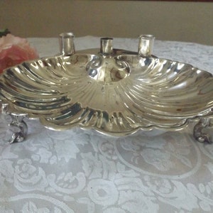 May include: A silver candlestick holder shaped like a seashell with three candle holders and three feet.