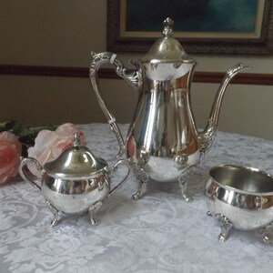 May include: A silver tea set with a teapot, creamer, and sugar bowl. Each piece has a decorative design and sits on three feet.