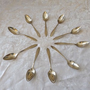 May include: A set of ten silver spoons arranged in a circular pattern on a white tablecloth with a floral design.