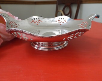 May include: A silver-plated, openwork bowl with two handles. The bowl has a scalloped edge and a decorative design of floral motifs. The bowl sits on a pedestal base.
