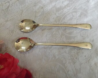 May include: Two silver serving utensils, a spoon and a fork, on a white background with a floral pattern.