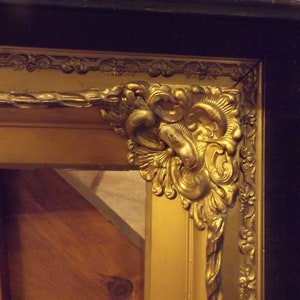 May include: A gold picture frame with ornate detailing and a black outer edge. The frame has a rope-like design and a decorative corner piece.