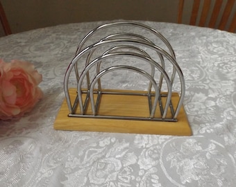 May include: A silver napkin holder with a wooden base. The holder has four arches that are designed to hold napkins.