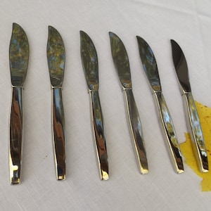 May include: Six silver butter knives with a slightly curved handle and a pointed tip.