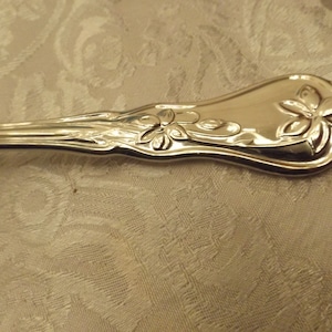 May include: Close-up of the handle of a silver spoon with a floral design. The handle is curved and has a raised design of flowers and leaves.