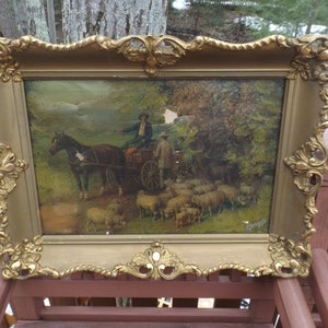 May include: A vintage framed oil painting depicting a man in a carriage pulled by a horse, with a flock of sheep in the background. The frame is ornate and gold-colored.