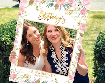 May include: A white photo booth prop with a gold frame and pink floral design. The text "Brittany's Bridal Shower August 28th, 2022" is printed on the bottom.
