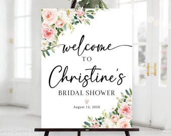 Puede incluir: Un letrero de bienvenida blanco para la despedida de soltera de Christine, exhibido en un caballete negro. El letrero presenta detalles florales en rosa y blanco, con el texto "welcome to Christine's bridal shower" en una elegante escritura. La fecha es el 12 de agosto de 202X.