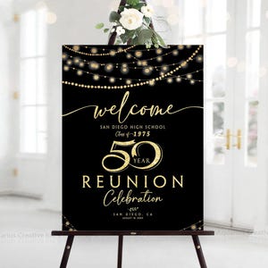 May include: A black sign welcoming guests to the San Diego High School Class of 1975's 50-year reunion. The sign has gold text and string lights, with the words "welcome," "50 YEAR REUNION Celebration," and the city and date.
