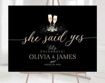 Puede incluir: Un cartel de fiesta de compromiso negro y dorado con el texto "she said yes let's celebrate! Olivia & James August 18, 202X" y un gráfico de dos copas de champán con vegetación.