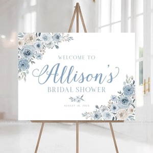 Op de afbeelding: Een wit welkomsbord met blauwe en cr&egrave;mekleurige bloemenontwerpen. Het bord luidt "Welkom bij Allison's Bridal Shower August 18, 202X".