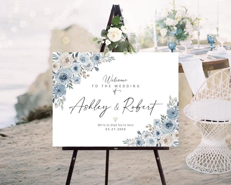 Peut inclure: Panneau de bienvenue de mariage blanc sur un chevalet noir, orn&eacute; de motifs floraux bleus. Le panneau indique "Bienvenue au mariage de Ashley & Robert" et la date 03.27.20XX. Un arrangement floral est plac&eacute; au-dessus du chevalet.