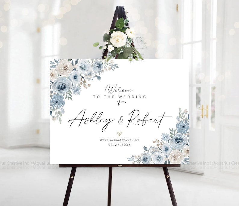 Peut inclure: Panneau de bienvenue de mariage blanc sur un chevalet noir, orn&eacute; de compositions florales bleues et blanches. Le panneau indique "Bienvenue au mariage de Ashley & Robert" et la date du 27.03.20XX.
