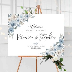 Peut inclure: Panneau de bienvenue de mariage blanc sur un chevalet en bois. Le panneau pr&eacute;sente des arrangements floraux dans des tons de bleu et de blanc. Le texte se lit &laquo;&nbsp;Bienvenue &agrave; notre mariage&nbsp;&raquo; et les noms &laquo;&nbsp;Veronica & Stephen&nbsp;&raquo;.