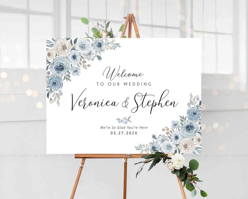 Peut inclure: Panneau de bienvenue de mariage blanc sur un chevalet en bois. Le panneau pr&eacute;sente des arrangements floraux dans des tons de bleu et de blanc. Le texte se lit &laquo;&nbsp;Bienvenue &agrave; notre mariage&nbsp;&raquo; et les noms &laquo;&nbsp;Veronica & Stephen&nbsp;&raquo;.