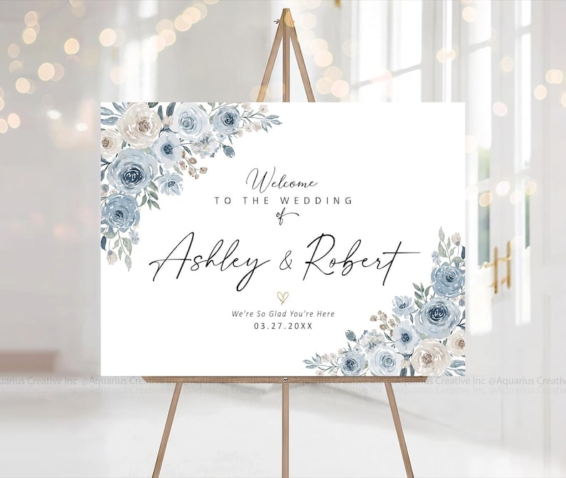 Peut inclure: Panneau de bienvenue de mariage blanc sur chevalet en bois. Il pr&eacute;sente des arrangements floraux bleus et cr&egrave;me. Le texte indique &laquo;&nbsp;Bienvenue au mariage de Ashley & Robert&nbsp;&raquo; et la date de l'&eacute;v&eacute;nement.
