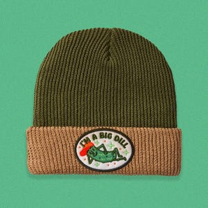 May include: Olive green and tan knit beanie with a patch that reads "I'm a Big Dill." The patch features a cartoon pickle wearing a red hat. The beanie is a comfortable, warm accessory.
