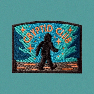 Puede incluir: Un parche bordado en negro y naranja con el texto "Cryptid Club" y una silueta de Bigfoot caminando en una escena de bosque azul y verde.